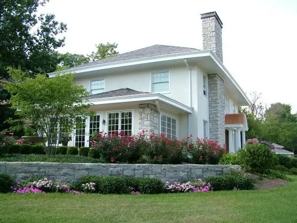 A stone and stucco Cincinnati home with a built stone retaining wall and rose plantings