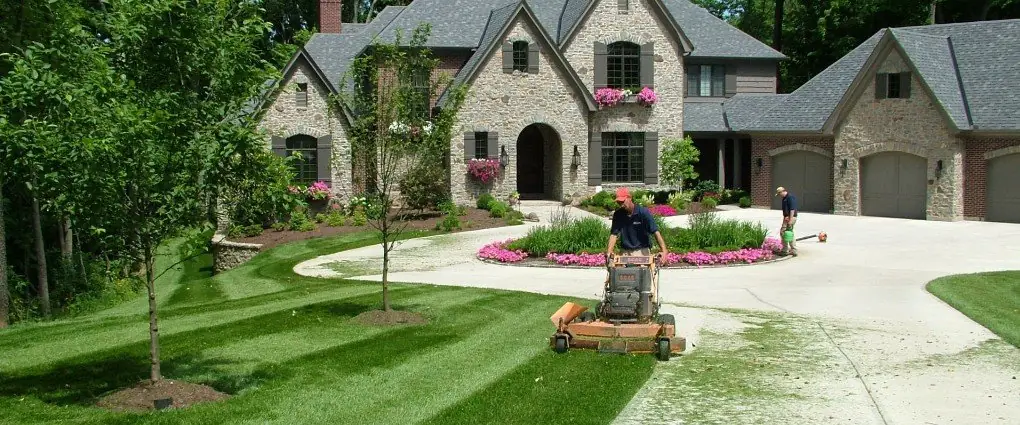 A Perrino Landscape crew member mowing the front lawn of a large stone estate home in Greater Cincinnati